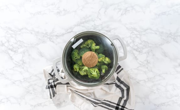 Flat lay. Steaming fresh broccoli in a cooking pot with a steamer basket to prepare steamed broccoli.