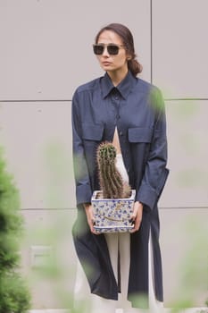 Woman tenderly standing in kimono with cactus in her hands on gray background. The girl seductively wear her robe. Fashionable details of kimono on grey background