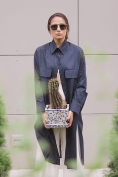 Woman tenderly standing in kimono with cactus in her hands on gray background. The girl seductively wear her robe. Fashionable details of kimono on grey background