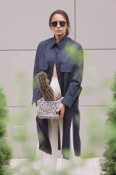 Woman tenderly standing in kimono with cactus in her hands on gray background. The girl seductively wear her robe. Fashionable details of kimono on grey background