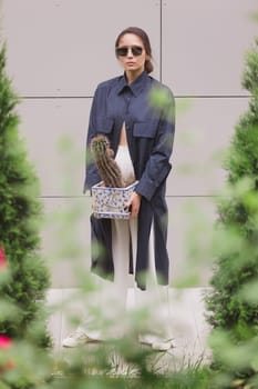 Woman tenderly standing in kimono with cactus in her hands on gray background. The girl seductively wear her robe. Fashionable details of kimono on grey background