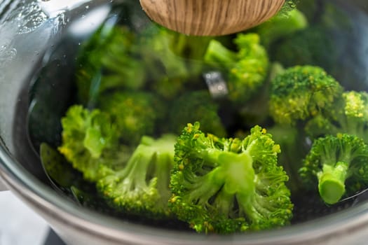 Steaming fresh broccoli in a cooking pot with a steamer basket to prepare steamed broccoli.