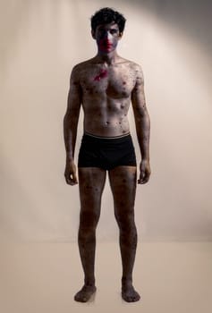 Scary male zombie standing on dark grey background, with white eyes and bloody mouth, looking at camera