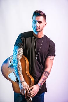 A young handsome man holding a guitar in his right hand in studio shot on neutral background. Photo of a man playing a guitar with passion and skill