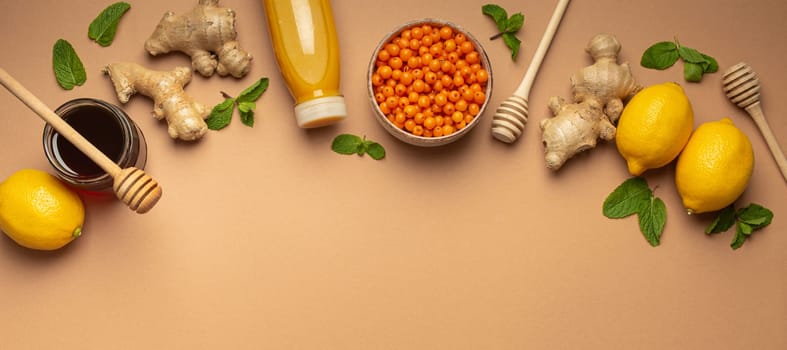 Lemons, mint, ginger, sea buckthorn berries, honey in glass jar, orange drink in bottle top view. Food for immunity stimulation and against flu. Healthy remedies to boost immune system, copy space.