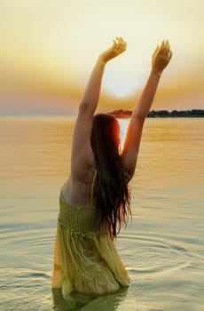 Attractive young woman with her arms raised above her head watches the sunrise on the sea.