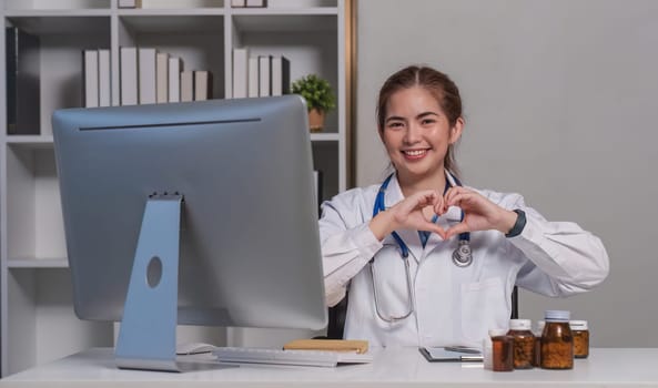 Beautiful asian woman wearing doctor uniform and stethoscope smiling in love doing heart symbol shape with hands. romantic concept..