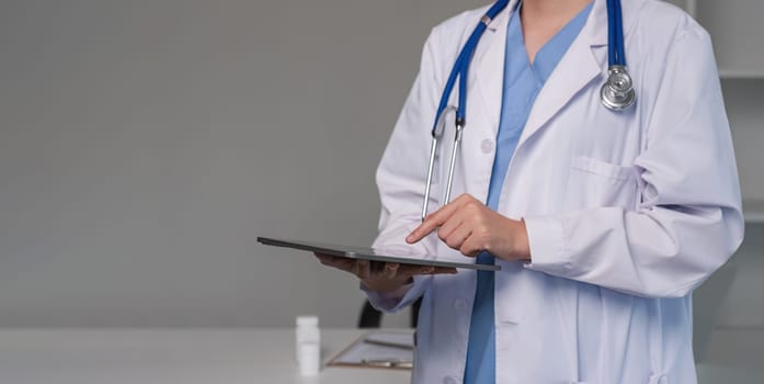 Close up female doctor holding a digital tablet wearing a medical coat and stethoscope in hospital.