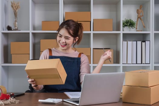Happy young Asian woman entrepreneur, Smile for sales success after checking order from online shopping store in laptop at home office, Concept of merchant business online and eCommerce.
