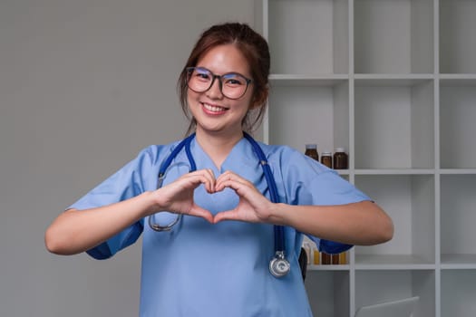 Beautiful asian woman wearing doctor uniform and stethoscope smiling in love doing heart symbol shape with hands. romantic concept..