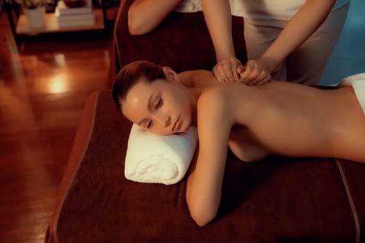 Caucasian couple customer enjoying relaxing anti-stress spa massage and pampering with beauty skin recreation leisure in warm candle lighting ambient salon spa at luxury resort or hotel. Quiescent