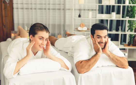 Caucasian couple customer enjoying relaxing anti-stress spa massage and pampering with beauty skin recreation leisure in day light ambient salon spa at luxury resort or hotel. Quiescent