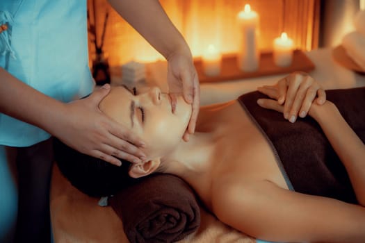 Caucasian woman enjoying relaxing anti-stress head massage and pampering facial beauty skin recreation leisure in warm candle lighting ambient salon spa in luxury resort or hotel. Quiescent