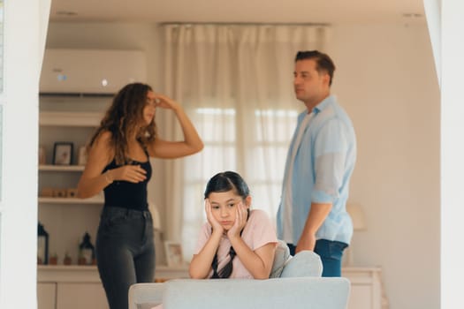 Annoyed and unhappy young girl look at camera, trapped in middle of tension by her parent argument in living room. Unhealthy domestic lifestyle and traumatic childhood develop to depression.Synchronos