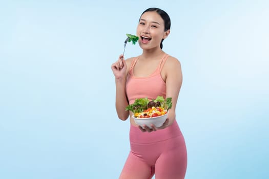 Young sporty Asian woman in sportswear holding salad bowl fill with vibrant of fruit and vegetable. Natural youthful and fit body lifestyle with balance nutrition on isolated background. Vigorous