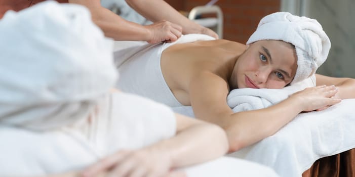 A portrait of two attractive young women with beautiful skin in white towel having a back massage by professional masseur at traditional spa salon. Beauty and healthy. Tranquility.