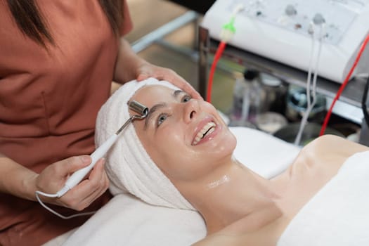 Beautiful caucasian woman lying on spa bed during having facial massage by professional hands at modern spa salon surrounded by beauty electrical equipment or medical equipment. Close up. Tranquility