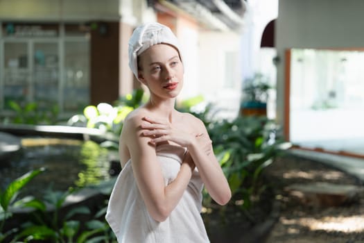 Attractive Caucasian woman with beautiful skin in white towel standing with confidence surrounded by natural environment at outdoor. Pretty girl standing while waiting for massage. Tranquility.