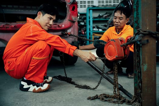 Mechanic testing strength and reliability of chain hoist for car towing in car workshop garage. Automotive service worker ensure through inspection of mechanical equipment. Oxus