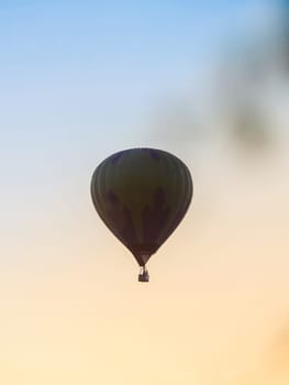 Hot Air Balloon silhouette at sunset sky background. Evening hot-air balloon flight with beautiful sunlight, view through tree branches. Romance of ballooning in a good weather.