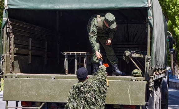 Soldiers unload firearms from a military truck. A soldier in the back of a truck.