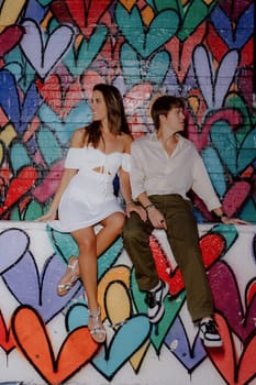 A couple kisses in front of a vibrant heart mural, symbolizing their love in a lively urban setting