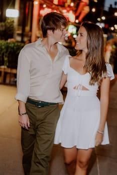 A couple happily enjoying a romantic and intimate walk together at night, dressed in stylish casual clothing