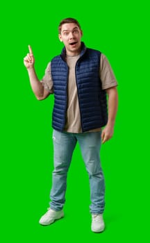Man in a navy vest gestures enthusiastically toward a green screen in studio