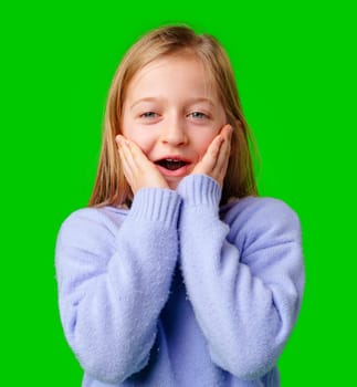 A young girl expresses surprise while smiling, with bright green background and cozy sweater