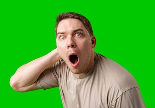 A surprised man stands in front of a bright green screen, expressing shock with his mouth open in studio