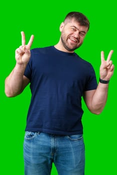 Man smiling and giving peace signs while standing against a bright green backdrop close up