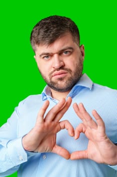 A man forming a heart shape with his hands against a vibrant green background close up