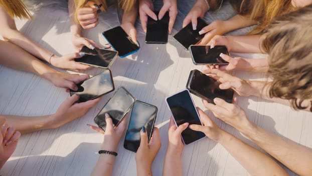 High school students gathered around a white table, using smartphones and sharing content during their summer break