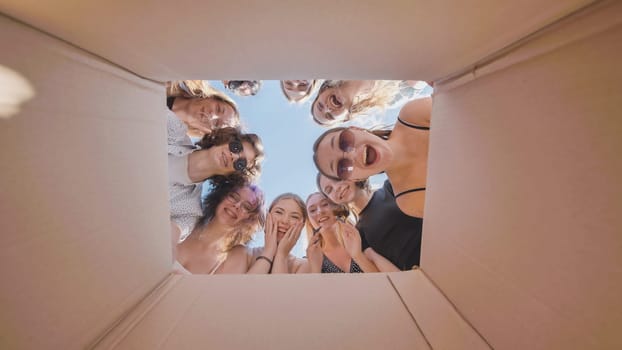 Group of excited female high school students looking inside a cardboard box, expressing surprise and happiness during their summer vacation