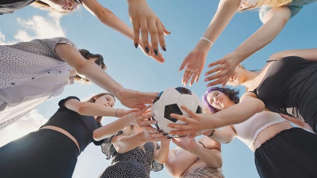 Group of teenage girls forming a circle with their hands holding a soccer ball, enjoying their summer vacation