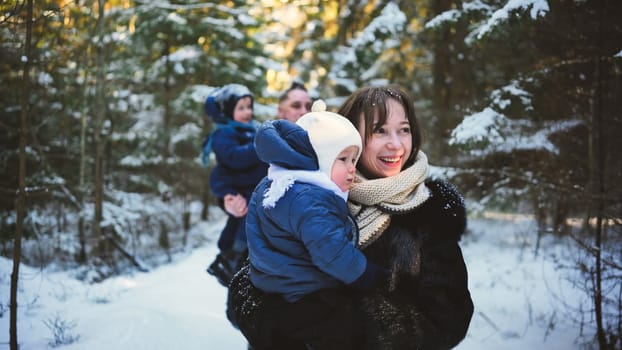 Cheerful family walking through snow covered woodland, parents and children smiling, sharing warmth and connection amid winter landscape
