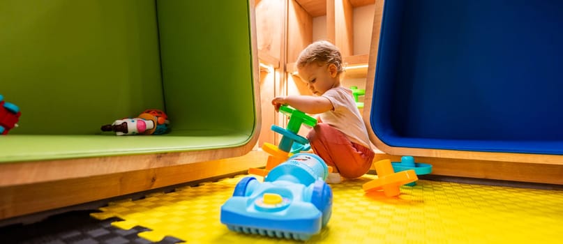 Little toddler exploring bright activity toys in a fun and safe playroom with shelves and creative spaces