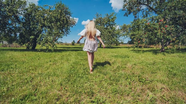 Blonde woman with long hair walking barefoot in a green meadow with apple trees, enjoying a sunny summer day in the countryside