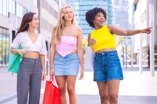 Three young women enjoying a sunny day, carrying shopping bags and smiling as they walk in an urban environment. Perfect for concepts like friendship, shopping, fashion, and lifestyle.