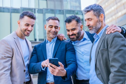 A group of confident businessmen standing outdoors in a modern urban setting. They are smiling and looking at a smartphone, symbolizing teamwork, technology, and connection.