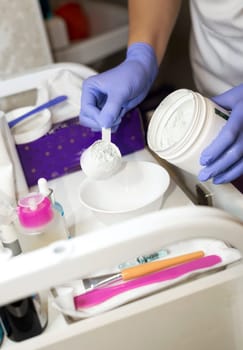A cosmetologist prepares a mask in her office. She prepares an alginate mask for a rejuvenation procedure. A close-up of her hands and the moment of preparation. She measures out a dose of powder with a measuring spoon.