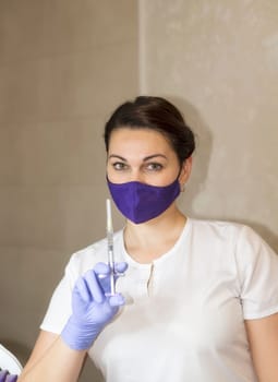 doctor in mask on face holds syringe in front of him. thin syringe is intended for cosmetic procedures. doctor in her office in mask and gloves. thin syringe is intended for cosmetic procedures.