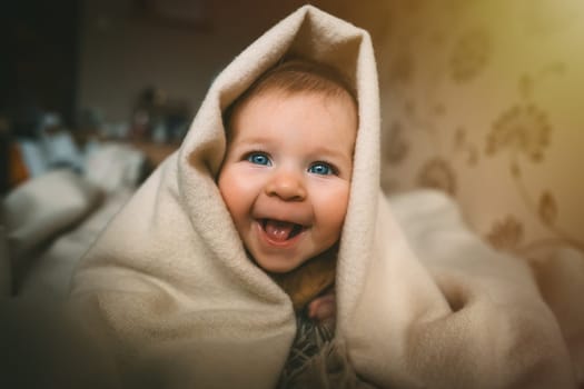 Smiling baby girl crawling on bed under the blanket. Adorable kid portrait. 5 month old child. Childhood concept. High quality photo