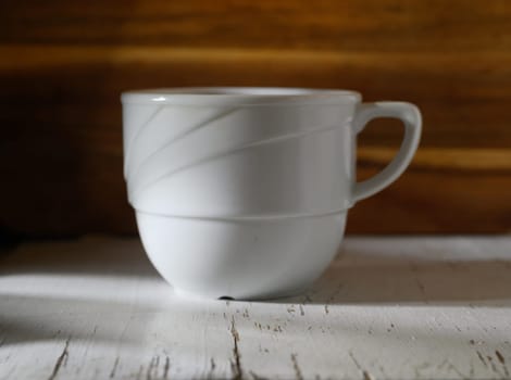 Delicate white cup sits gracefully on weathered wood, illuminated by gentle natural light filtering through a window.