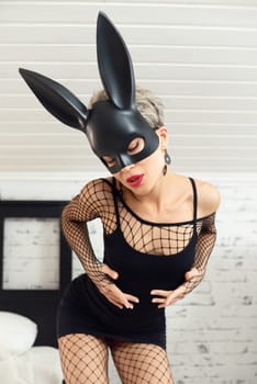 Sexy girl in a short black dress and a rabbit mask from a sex shop poses erotically in mesh bodysuit