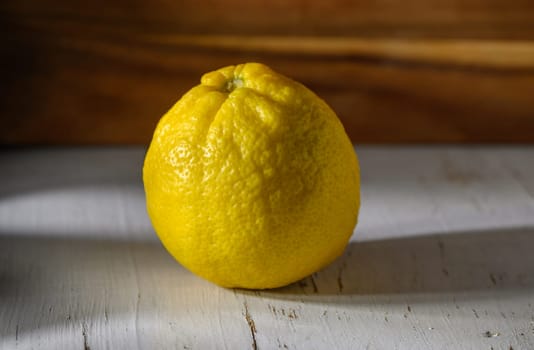 A vibrant yellow lemon sits alone on a weathered wooden surface, illuminated by gentle sunlight.