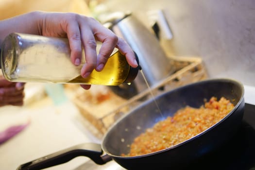 Pouring olive oil over sauted vegetables in a frying pan