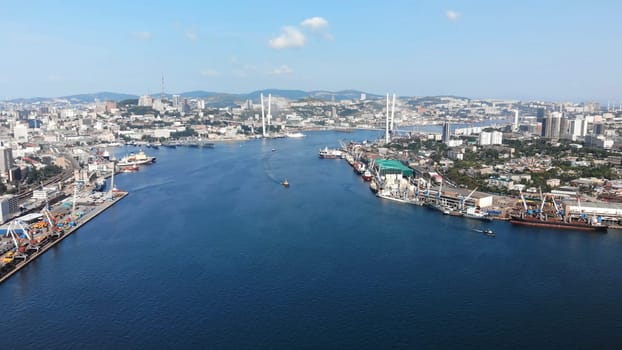 Aerial cityscape of vladivostok, russia, featuring zolotoy rog bay, industrial and commercial ships, and the cable stayed zolotoy bridge on a sunny day