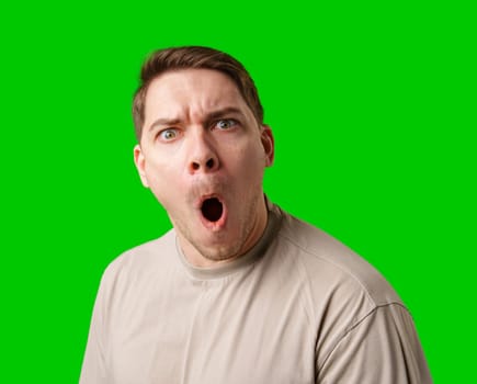 A surprised man stands in front of a bright green screen, expressing shock with his mouth open in studio