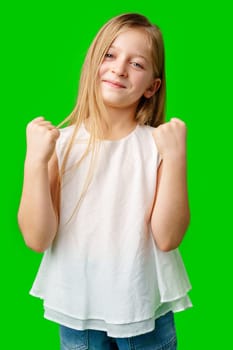 Happy child celebrating success with joyful fist pump in front of bright green background in studio
